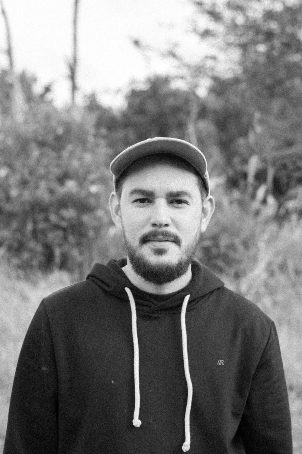 Black-and-white outdoor portrait of a Coocine member wearing a cap