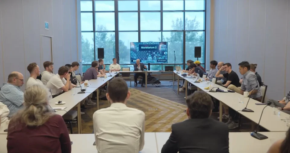 A roundtable at Monetarium 2 with the illustrated identity on the screen, from the Highlights film