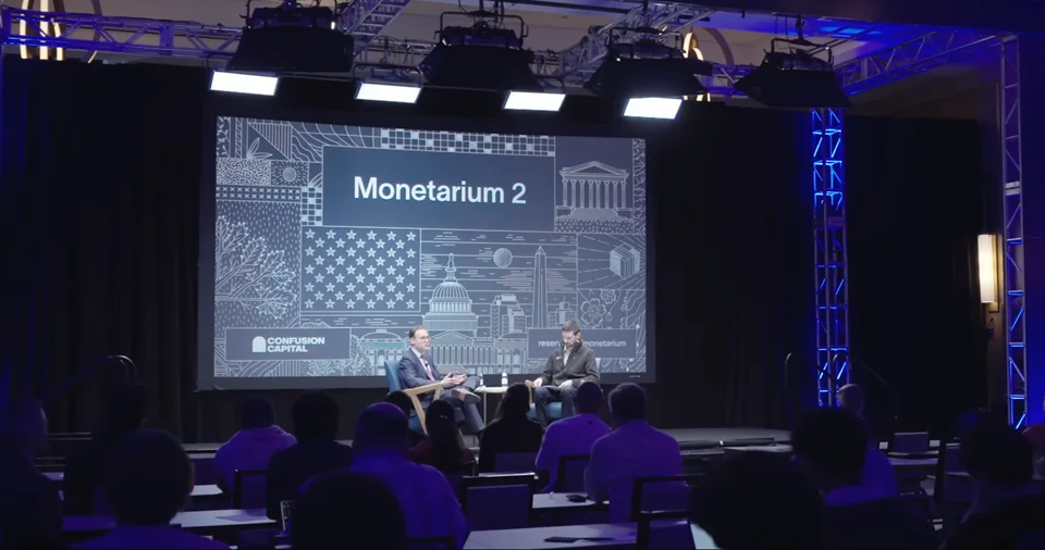 Monetarium 2 stage in Washington: two speakers seated in front of the illustrated backdrop