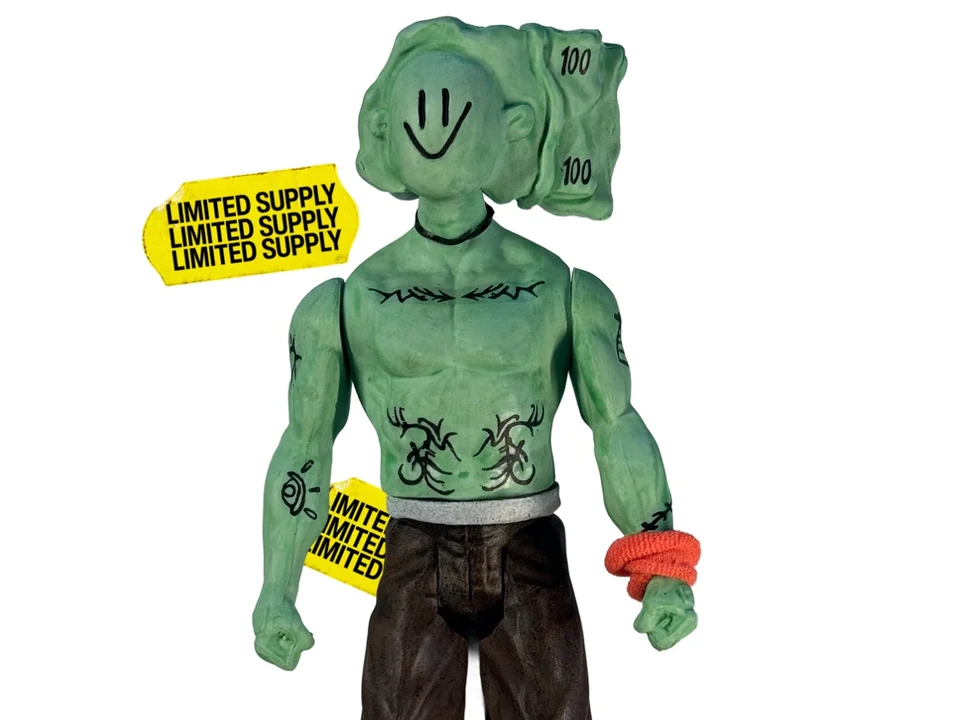 Uglyman, the UGLYCASH action figure: close view of its smiling banknote-shaped head and tattooed torso